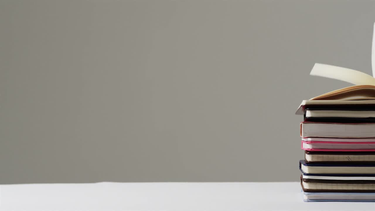 primer plano de un libro abierto en una pila de libros con espacio de copia en fondo gris, en cámara lenta