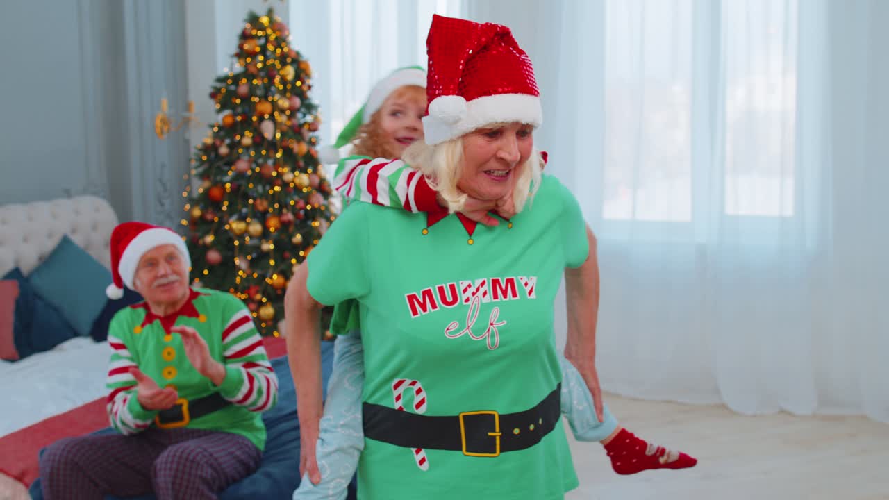 Grandmother carrying small girl toddler kid playing piggyback ride game at home christmas bedroom