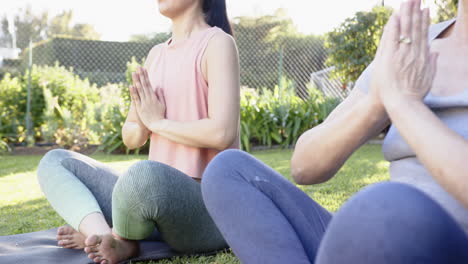 practicing yoga, asian grandmother and granddaughter sitting cross-legged on mats in garden