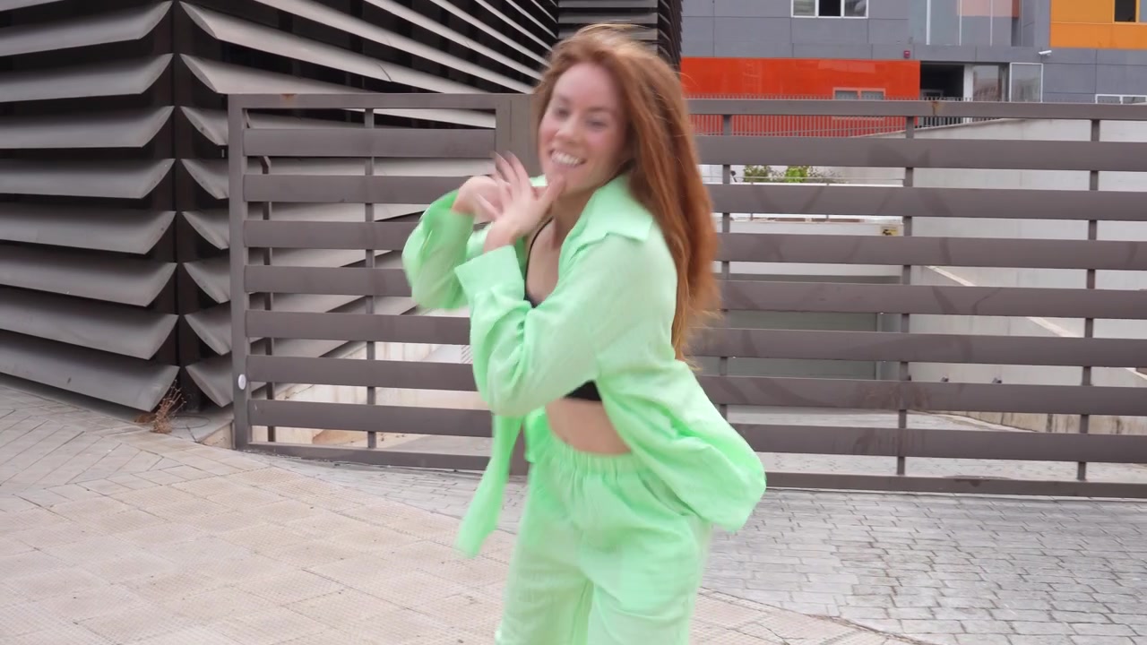 Uma jovem alegre em um conjunto verde dançando feliz ao ar livre perto de um edifício moderno.