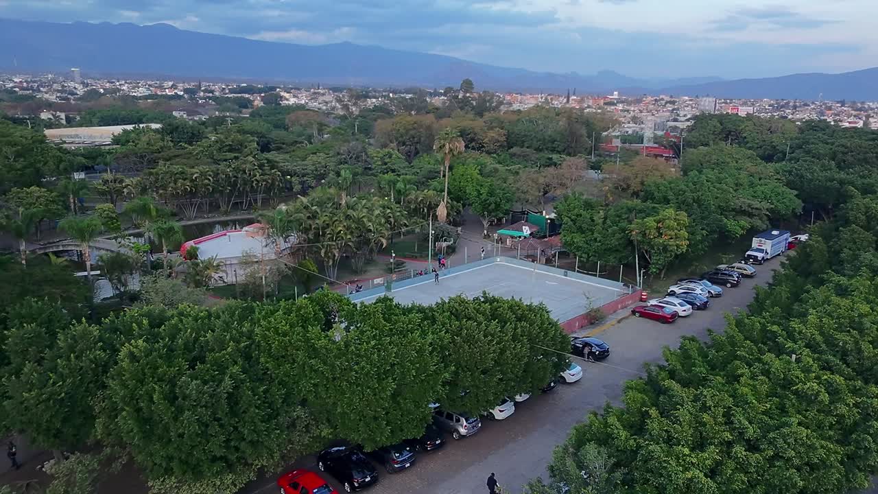 Aerial: Park Alameda at sunset with trees and cars in Jiutepec, Morelos, Mexico, establishing drone shot