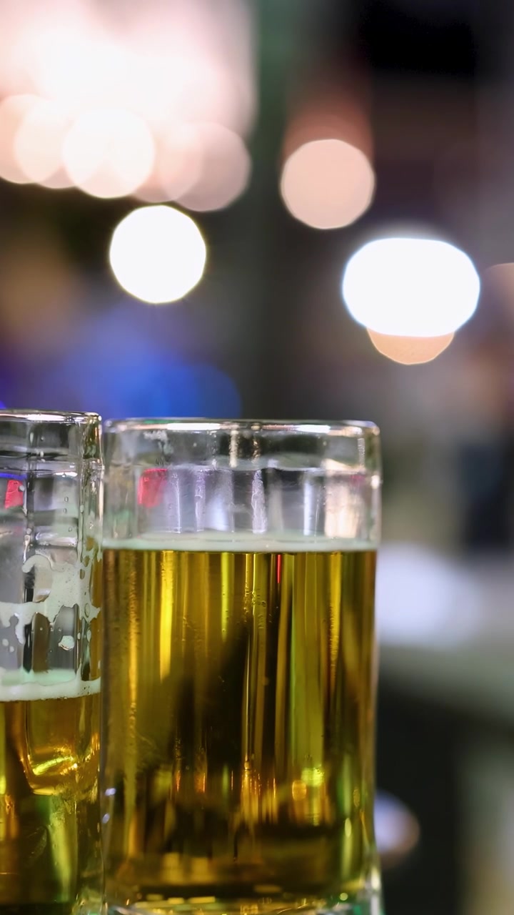Scena notturna sfocata con bicchieri di birra a fuoco, che cattura movimento e luci vivaci in un ambiente animato.