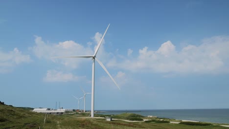 wind turbine at the coast rotating slowly with sea and clouds in background