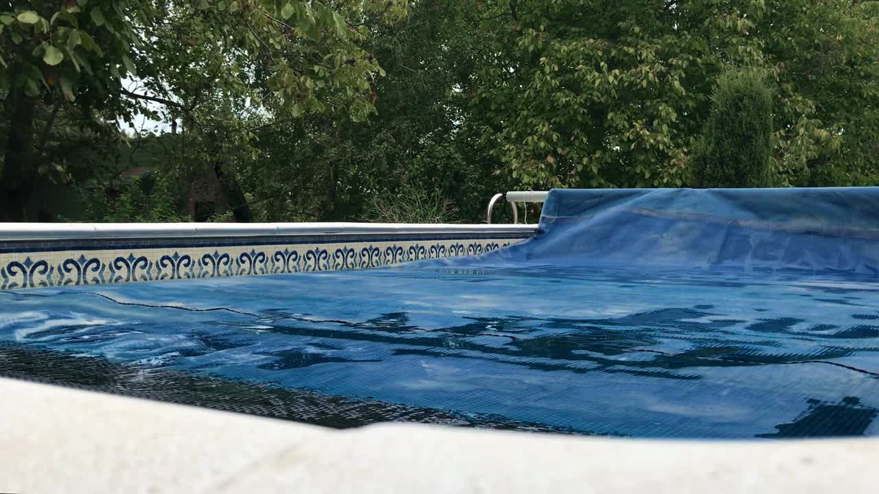 Gradual swimming pool solar reel thermal cover removal with lush greenery background