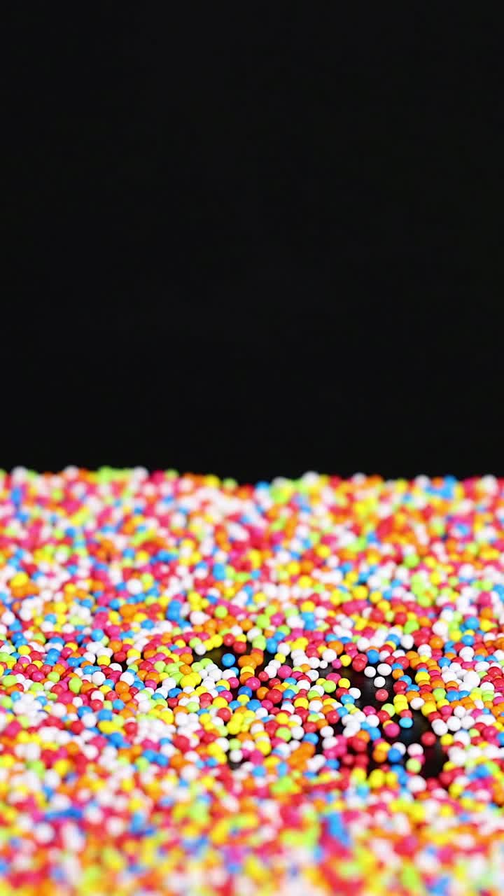 Vibrant sprinkles cascade onto a black surface