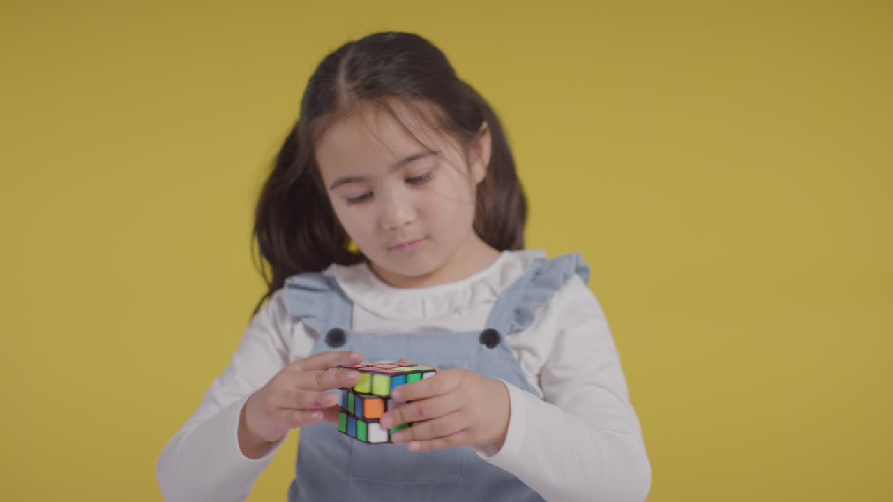 노란색 배경에 퍼즐 큐브를 해결하는 asd 스펙트럼에 있는 어린 소녀의 스튜디오 초상화