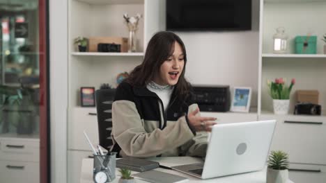 The-young-woman-happily-chats-with-someone-on-her-laptop,-smiling-and-commenting