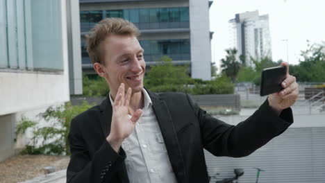 Smiling-man-having-video-chat-on-phone-waving-hand,-chewing-gum