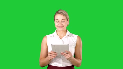 beautiful girl holding a tablet touch pad computer gadget swiping pages and looking in camera on a green screen, chroma key