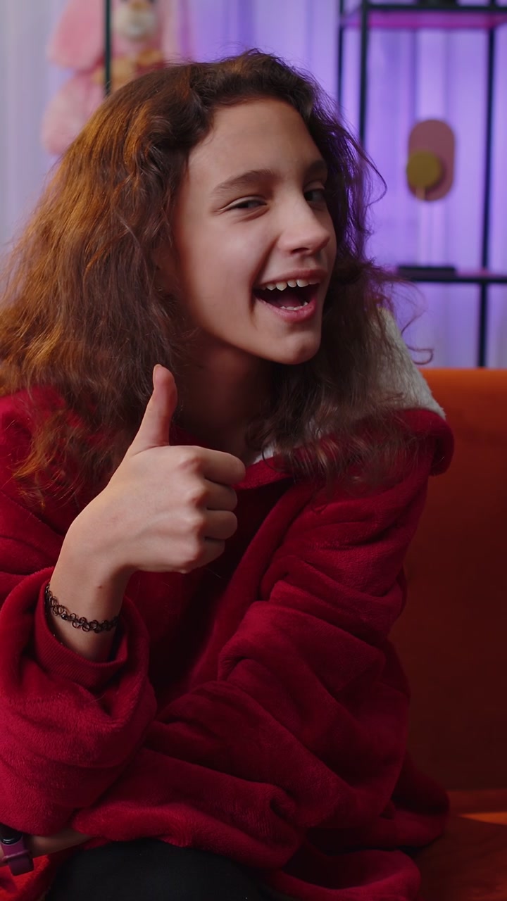 Ragazza felice che guarda con approvazione la telecamera mostrando i pollici in alto come un segno positivo di buone notizie