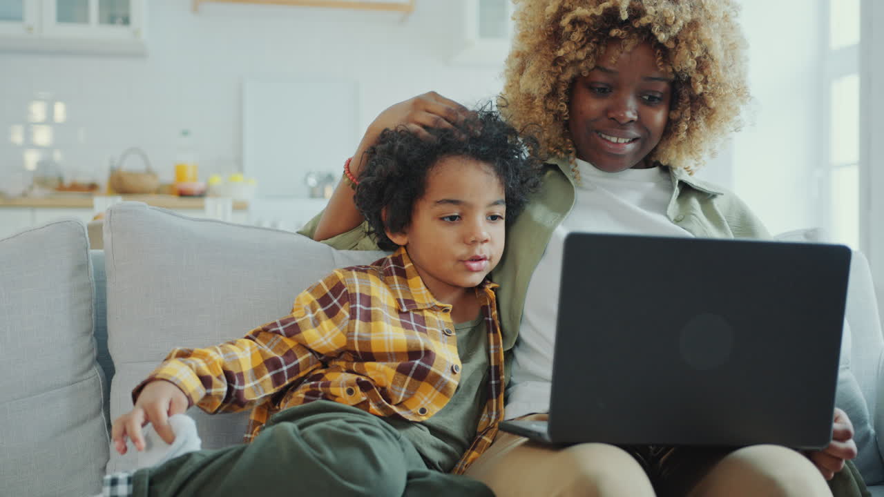 Mother and Little Son Bonding on Sofa and Discussing Something on Laptop Screen