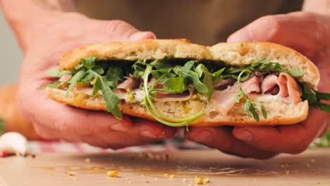 mortadella ham sandwich, traditional italian focaccia filled with thin pesto slices of mortadella, served by chef man in cafe restaurant. macro of traditional italian spanish tapas antipasti.