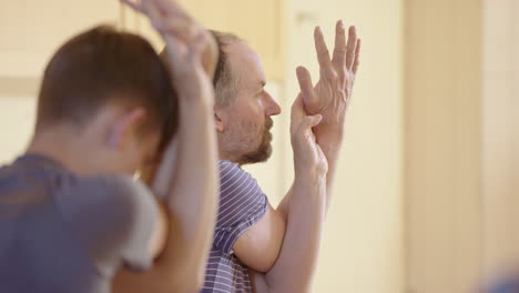 yogi men in eagle pose gripping palm and thumb in yoga class, telephoto