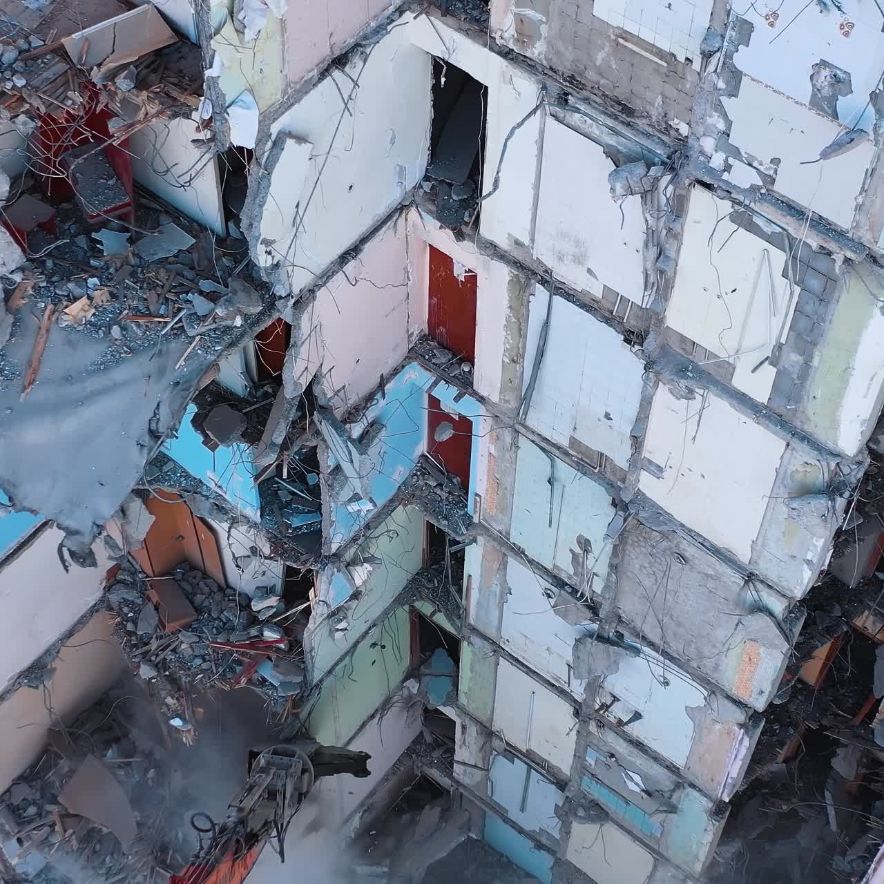 Huge building being demolished with the help of a tractor. Excavator with a long claw breaking walls of the ruined building. View from the above