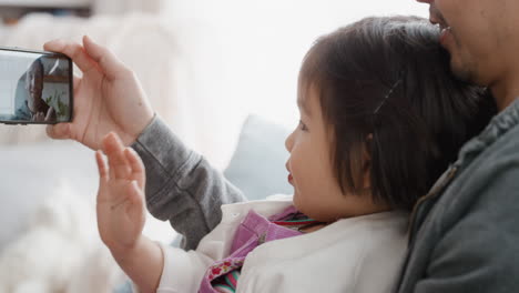 Padre-Asiático-Y-Niño-Usando-Un-Teléfono-Inteligente-Teniendo-Video-Chat-Niña-Saludando-Compartiendo-El-Fin-De-Semana-Con-Papá-Disfrutando-Charlando-Por-Teléfono-Móvil-Con-Un-Amigo-4k