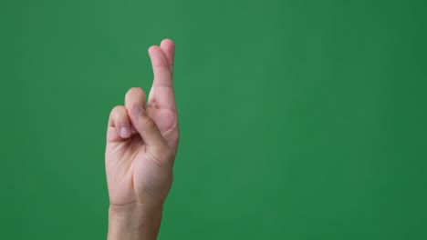 hand with fingers crossed over green screen