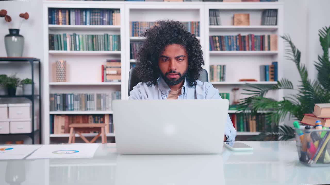 Young arabian man working with laptop picks up phone and makes frightened look