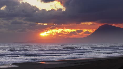 dramatic sunrise breaking through gray clouds over stormy ocean waves, beach view, coastal seascape background, costa blanca, spain, wide shot