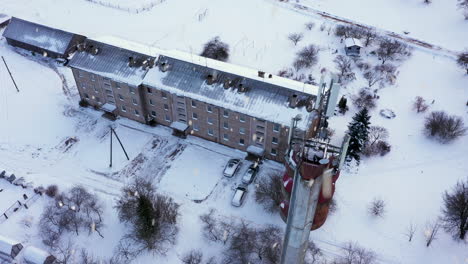 Pequeño-Edificio-De-Apartamentos-Y-Torre-Alta-De-Telecomunicaciones-En-Temporada-De-Invierno-Durante-Las-Nevadas,-Tiro-Aéreo-Ascendente