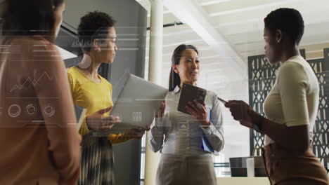 Animation-of-globe,-graphs,-loading-bars-and-circles,-diverse-female-coworkers-discussing-in-office