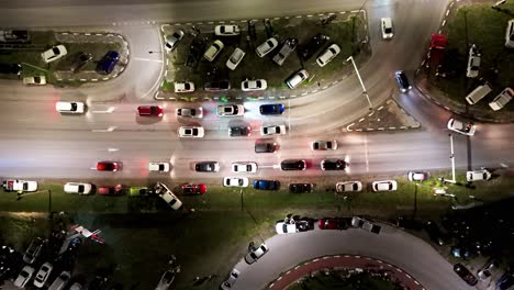 detenerse en el semáforo de circunvalación de los coches de curva por la noche con vehículos estacionados en el césped, aéreo