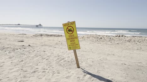 Manténgase-Alejado-Del-Agua-Contaminada-Con-Aguas-Residuales,-Tenga-Cuidado-Con-El-Letrero-En-Imperial-Beach,-California,-Día-Soleado:-Cámara-Lenta-Con-Muelle