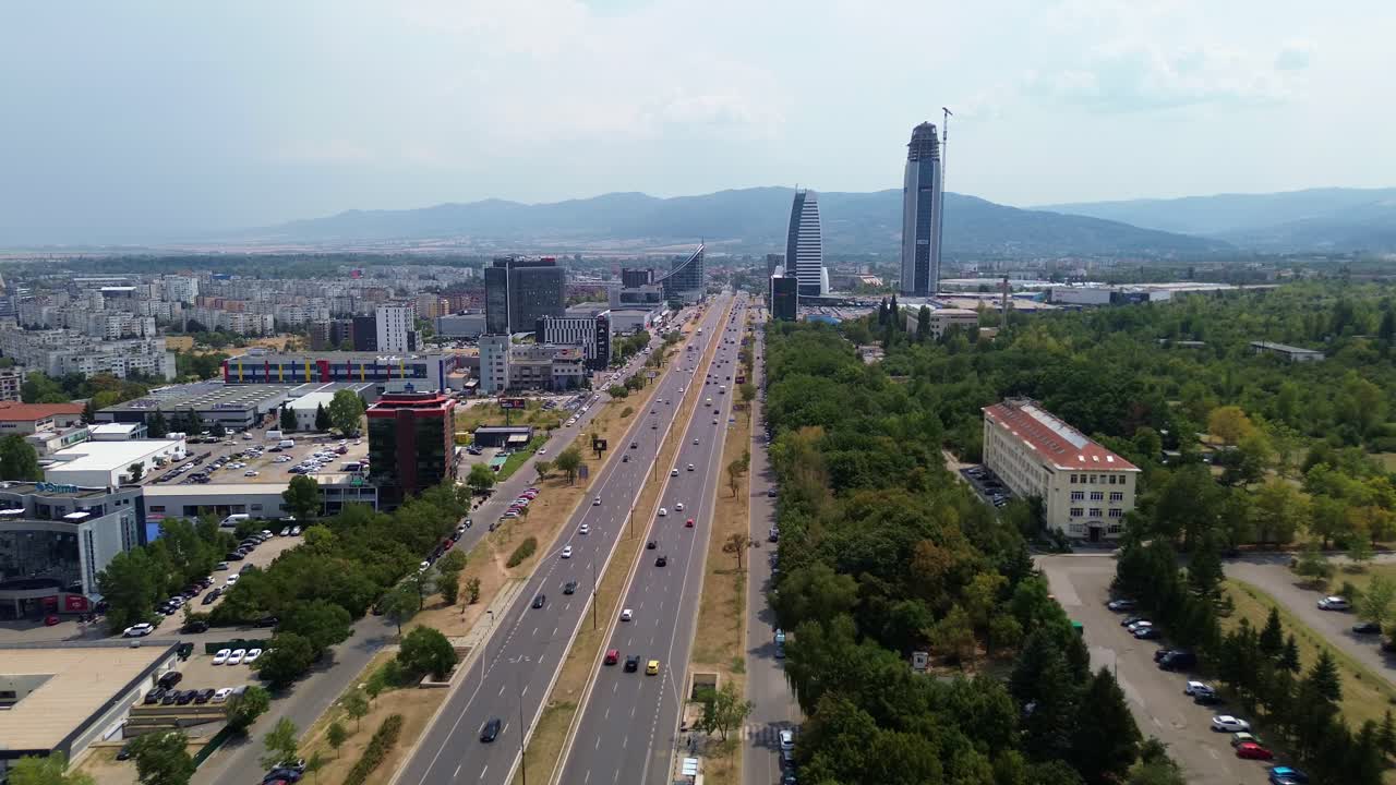 drone shot, showing off the car traffic on 'Tsarigradsko shose', one of the main boulevards in Sofia, the capital of Bulgaria, many cars driving on the road, a couple of skyscrapers in the background