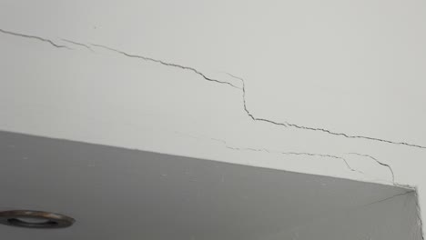 closeup crack in white wall panning left, home repair, home insurance, broken wall, fixing required, 4k