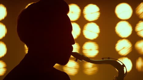 silhouette guy blowing saxophone on stage closeup. young saxophonist performing.