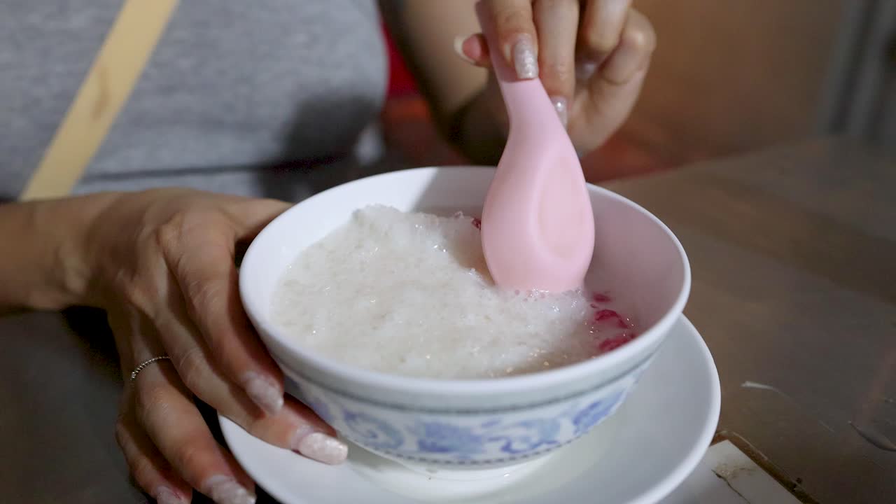 Hand uses pink spoon to scoop traditional Thai dessert with coconut milk and red rubies
