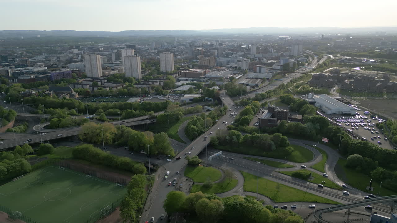 Vista aerea ad angolazione elevata che mostra il flusso intenso del traffico sulle autostrade urbane con lo skyline della città di Glasgow e gli edifici residenziali sullo sfondo