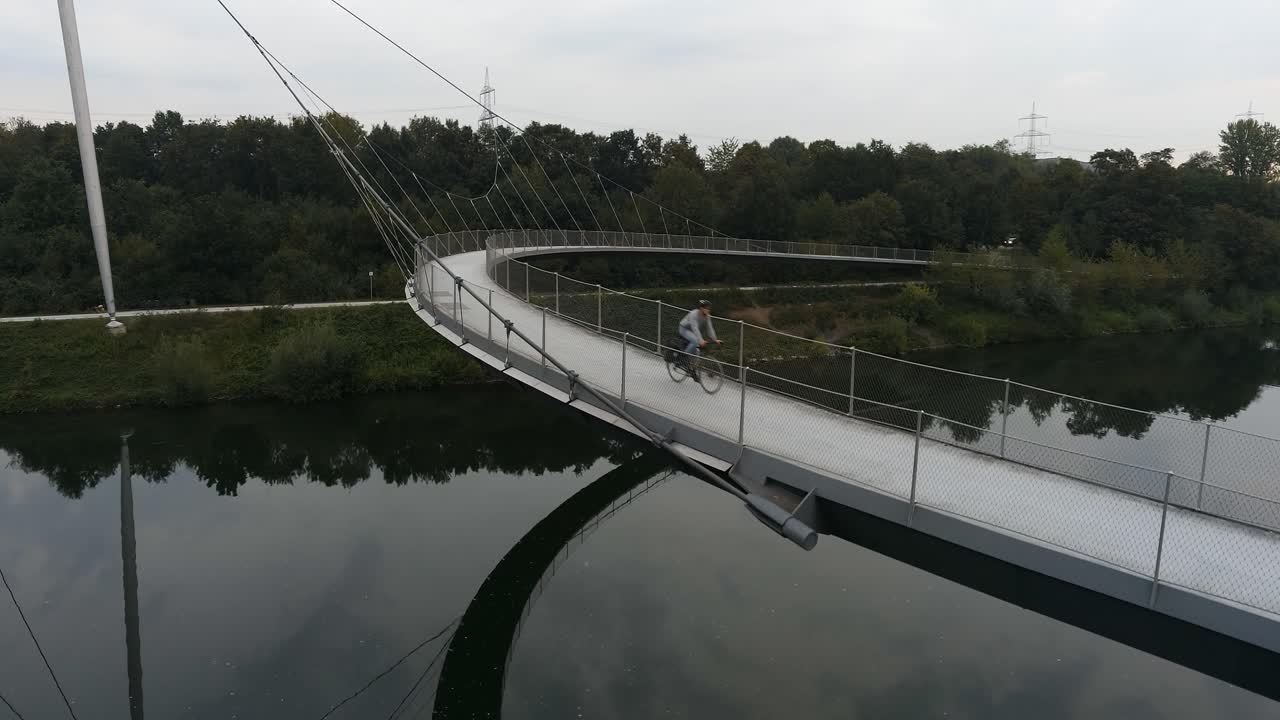 A person walking and cycling on a modern curved bridge over water