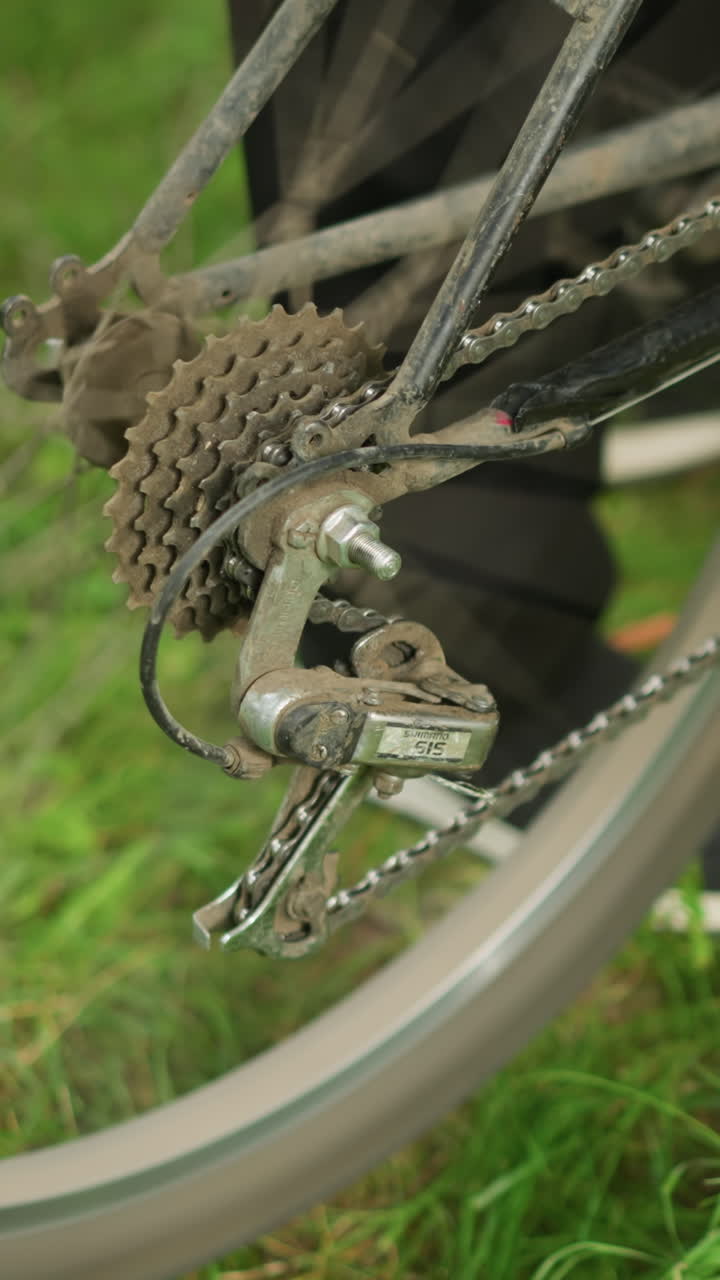 primer plano de alguien de pie al lado de una bicicleta estacionada en un campo de hierba, ajustando el pedal hacia atrás, levantando el neumático trasero, pedaleando para girar las ruedas y bajando suavemente la bicicleta hacia abajo