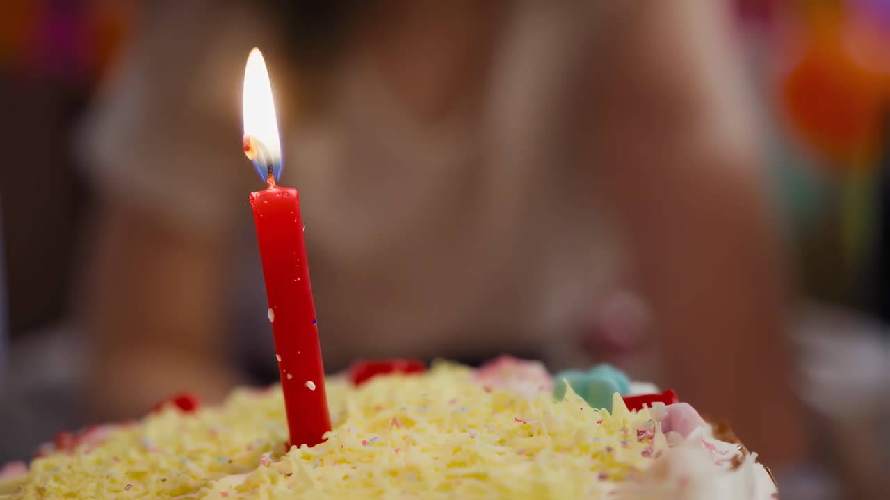 Birthday girl gazing intently at single red candle burning atop decorated cake, capturing magical moment of childhood celebration and anticipation of making special wish