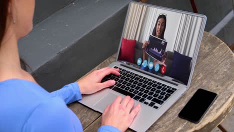 mujer de negocios caucásica sentada en un escritorio usando una computadora portátil haciendo una videollamada con una colega
