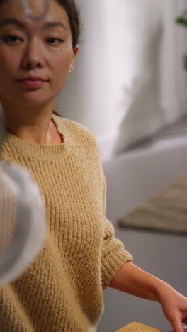 vertical video close up of woman at home in kitchen preparing healthy vegetarian or vegan meal putting sliced tofu on board into pan