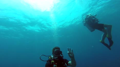 Taucherpaar,-Das-Direkt-Unter-Der-Meeresoberfläche-Schwimmt,-Wobei-Einer-Einem-Mittaucher-Ein-Zeichen-Gibt