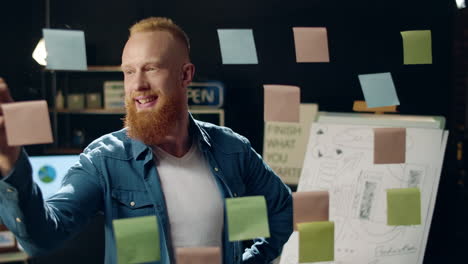 un hipster sonriente recogiendo ideas en la oficina. un hombre de negocios quitando una pegatina.
