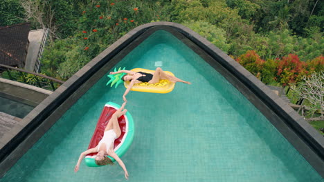 two-women-floating-in-swimming-pool-lying-on-inflatables-best-friends-having-fun-summer-day-on-vacation-at-tropical-hotel-resort-wearing-bikinis-top-view