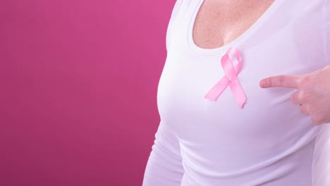 video of midsection of caucasian woman wearing pink cancer awareness ribbon, with pink background