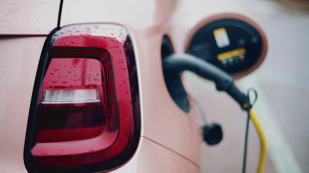 Close up of a pink, electric car charging outdoors under rain