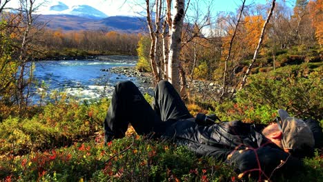 Excursionista-Tomando-Un-Descanso-Acostado-Junto-A-Un-Río,-Observando-El-Paisaje-Escénico-En-Abisko,-Laponia-En-El-Norte-De-Suecia