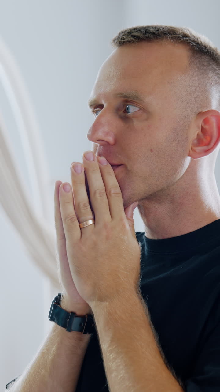 Man is holding hands in front of his face in praying position. Worried husband portrait during the childbirth of his baby in hospital ward. Vertical video