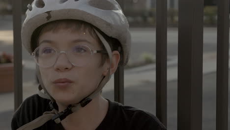 cute kid sitting outside at golden hour with a bike helmet on and glasses smiles a big smile