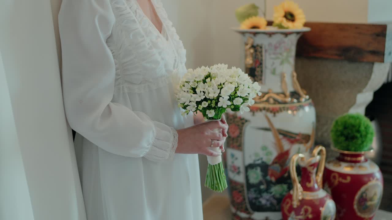 novia sosteniendo un ramo de flores blancas al lado de jarrones ornamentados en el interior