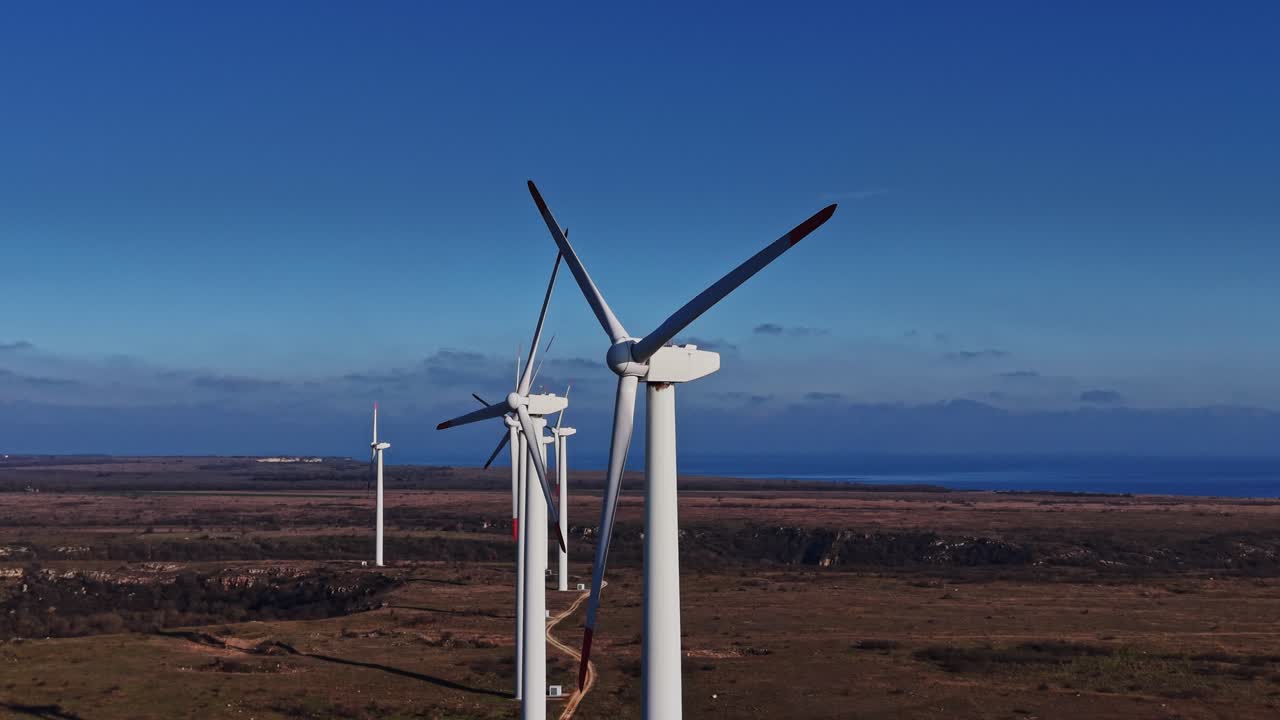 Le turbine eoliche si ergono sulla terraferma vicino alla costa sotto un cielo blu
