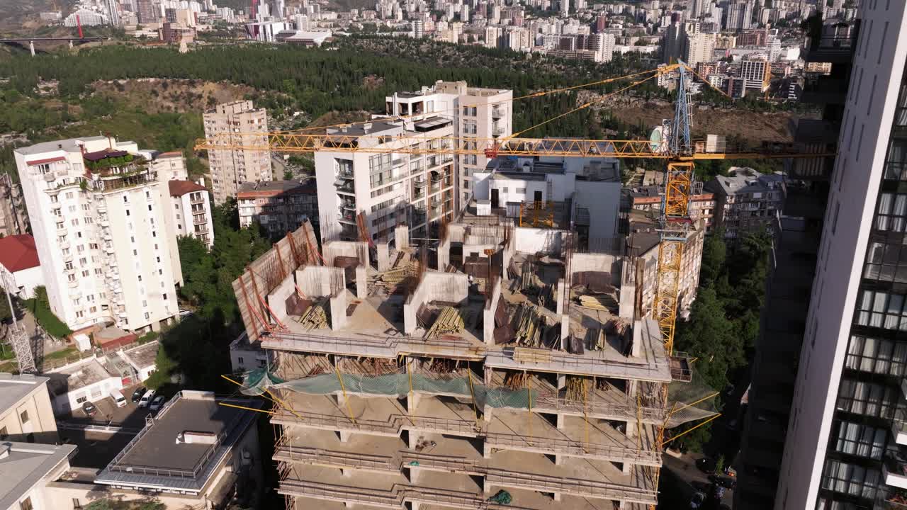 Aerial Establishing Shot of New Skyscraper Under Construction, Exposed Concrete and Steel Beams and Various Construction Materials, next to a completed Modern Skyscraper