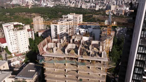 aerial establishing shot of new skyscraper under construction, exposed concrete and steel beams and various construction materials, next to a completed modern skyscraper