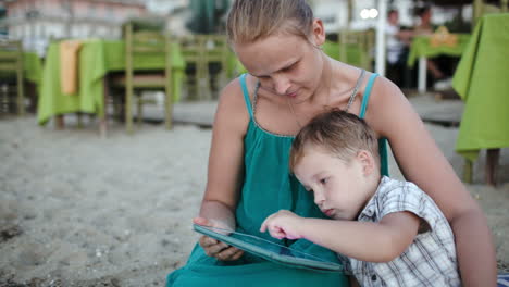 mother and son using tablet pc near beach cafe