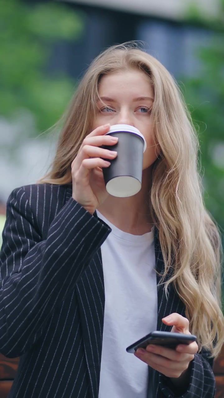 Ung kvinde bruger smartphone og drikker kaffe udendørs